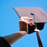 Girl is holding graduation cap up in the air against blue sky